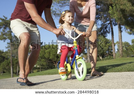 Parents Teaching Daughter To Ride Bike In Park