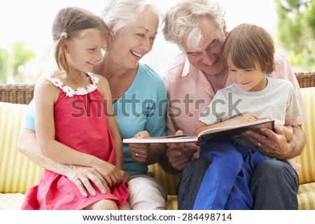 Grandparents And Grandchildren Reading Book On Garden Seat