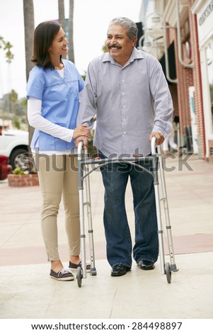 Carer Helping Senior Man To Use Walking Frame