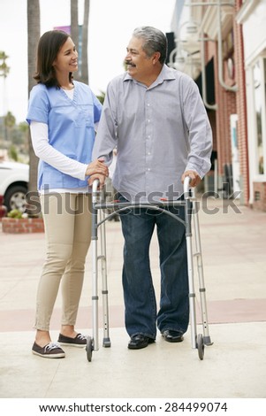 Carer Helping Senior Man To Use Walking Frame