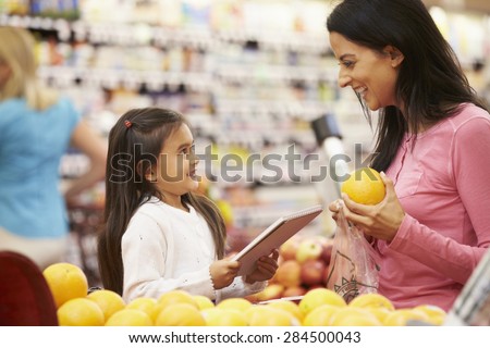 Mother And Daughter At Fruit Counter In Supermarket With List