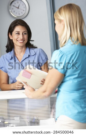 Female Patient With Receptionist In Doctors Waiting Room