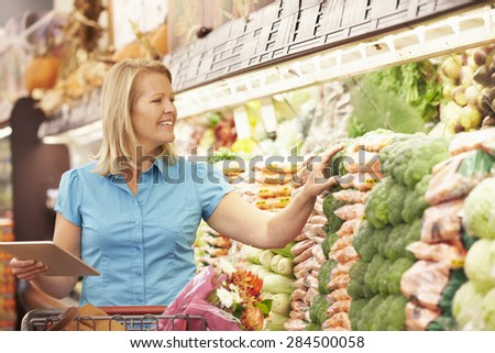 Woman Reading Shopping List From Digital Tablet In Supermarket