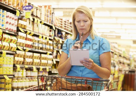 Woman In Grocery Aisle Of Supermarket With List