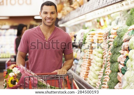 Man Pushing Trolley By Produce Counter In Supermarket