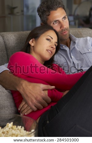 Hispanic Couple On Sofa Watching TV And Eating Popcorn