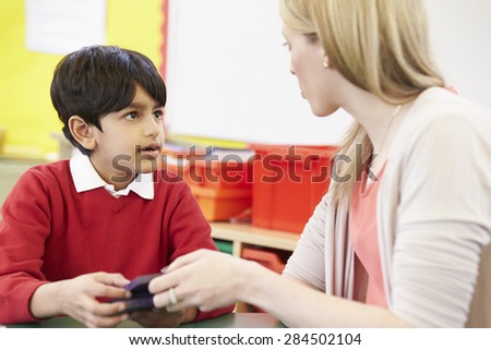 Teacher Helping Male Pupil With Maths At Desk