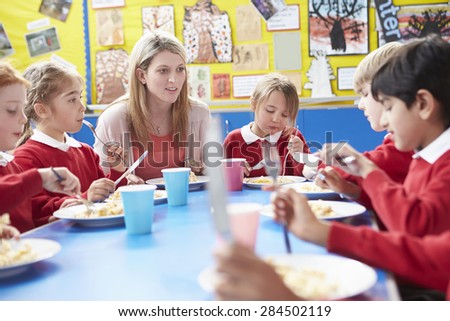 Schoolchildren With Teacher Sitting At Table Eating Lunch