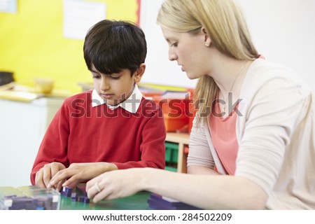 Teacher Helping Male Pupil With Maths At Desk