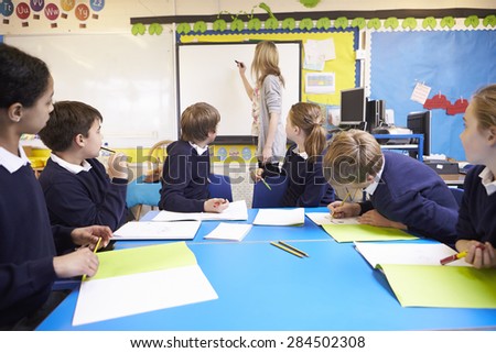 Pupils Sitting At Table As Teacher Stands By Whiteboard