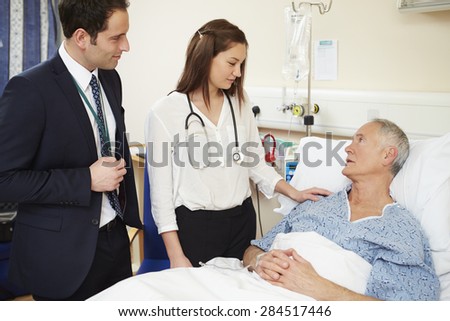 Medical Staff On Rounds Standing By Male Patient\'s Bed