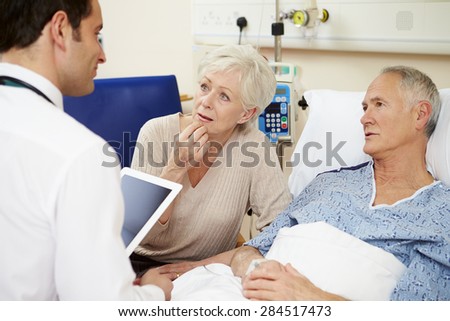 Doctor With Digital Tablet Talking To Couple By Hospital Bed