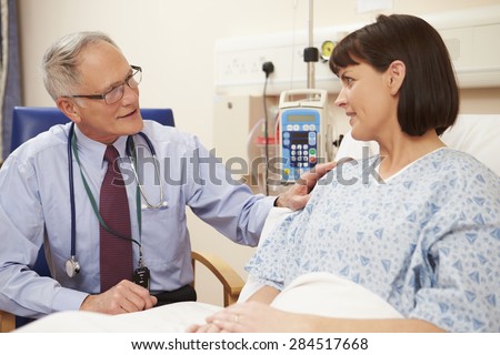 Doctor Sitting By Female Patient's Bed In Hospital