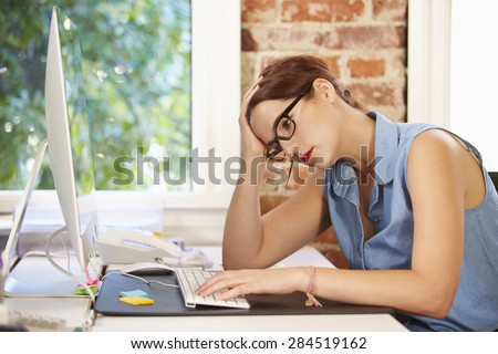 Stressed Businesswoman Working At Computer In Modern Office