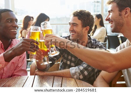 Three Male Friends Enjoying Drink At Outdoor Rooftop Bar