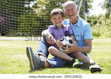 Grandfather And Grandson Playing Football In Garden