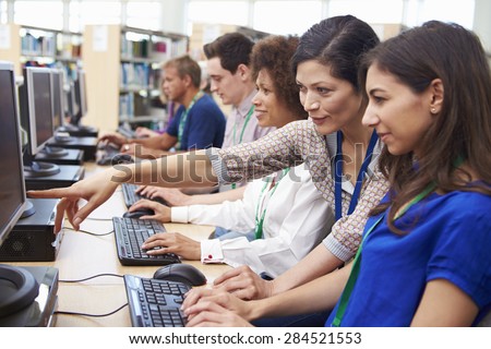 Group Of Mature Students Working At Computers With Tutor