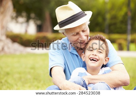 Grandfather And Grandson Sitting In Park Together