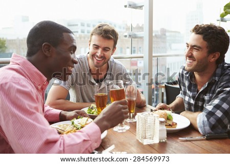 Three Male Friends Enjoying Lunch At Rooftop Restaurant
