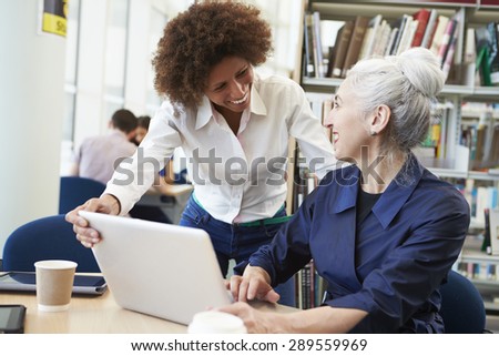 Teacher Helping Mature Student With Studies In Library