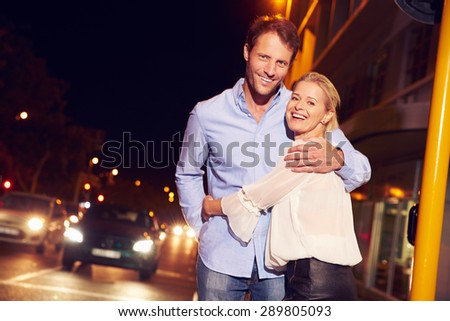 Couple embracing on city street at night, portrait