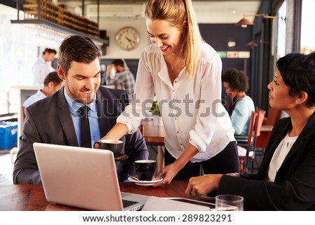 Two business people with laptop being served in a cafe