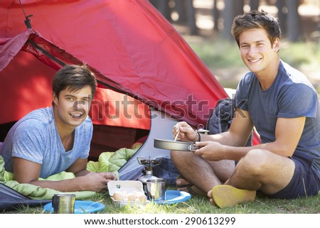 Two Young Men Cooking On Camping Stove Outside Tent