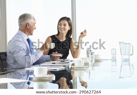 Two Business Colleagues Sitting Around Boardroom Table Having Informal Discussion