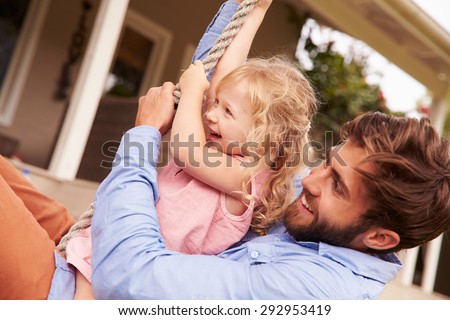 Father playing with daughter on a rope swing in a garden