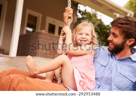 Father playing with daughter on a rope swing in a garden