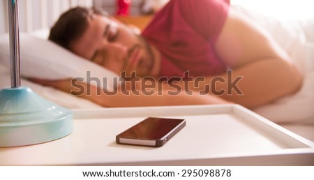 Man Asleep In Bed Using Alarm On Mobile Phone