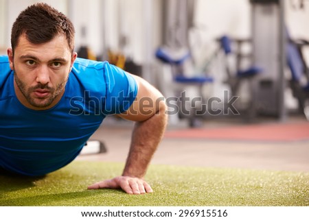 Young man doing push ups at a gym, looking to camera, copy space