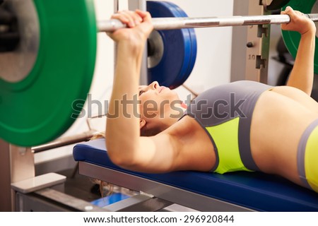 Young woman with barbells bench pressing weights