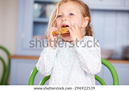 Young Girl Sitting At Table Eating Cookie