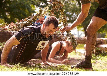 Assault course competitor helping others crawl under nets