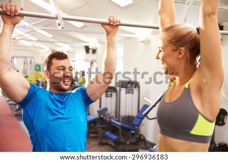 Man and woman reaching up to monkey bars at a gym