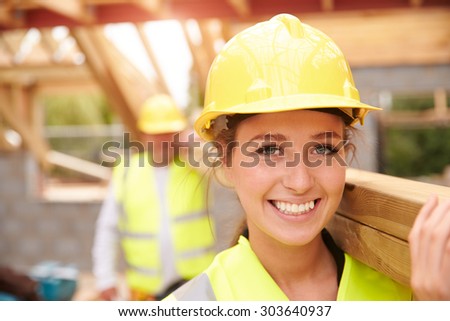 Builder And Female Apprentice Carrying Wood On Site