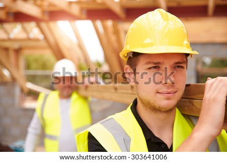 Builder And Apprentice Carrying Wood On Construction Site