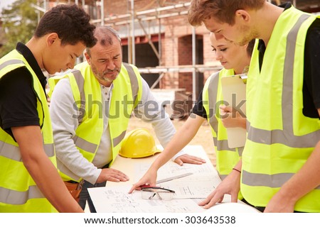 Builder On Building Site Discussing Work With Apprentice
