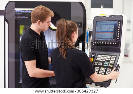Two Young Engineers Operating CNC Machinery On Factory Floor
