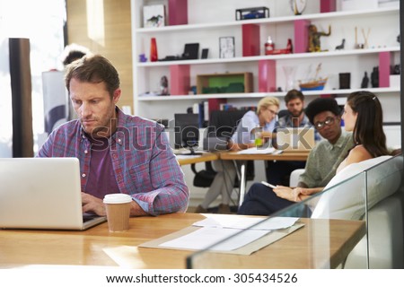Businessman Working On Laptop In Busy Office