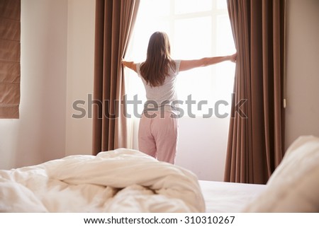 Woman Standing By Bedroom Window And Opening Curtains