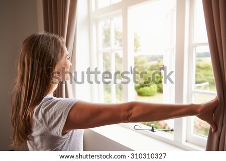 Woman Standing By Bedroom Window And Opening Curtains