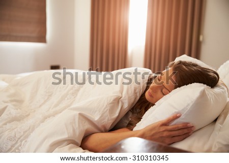 Woman Asleep In Bed As Sunlight Comes Through Curtains