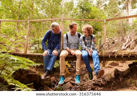 Grandfather, father and son sitting on a bridge in a forest