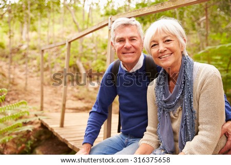 Happy senior couple sitting on a bridge in forest, portrait