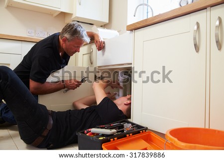 Plumber teaching a young apprentice to fix a kitchen sink