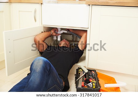 A plumber lying on his back to fix a kitchen sink