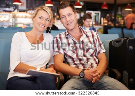 Couple In Airport Departure Lounge Waiting To Go On Vacation