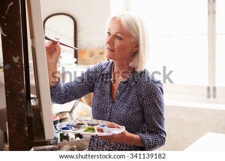 Senior Female Artist Working On Painting In Studio